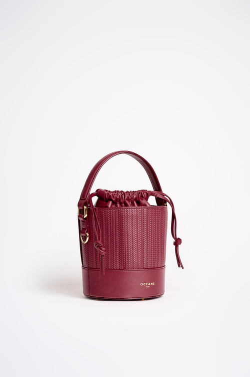 Borsa a secchiello Grace di Oceane Paris in pelle bordeaux, vista di tre quarti con manico, dettagli intrecciati e cordoncini laterali.