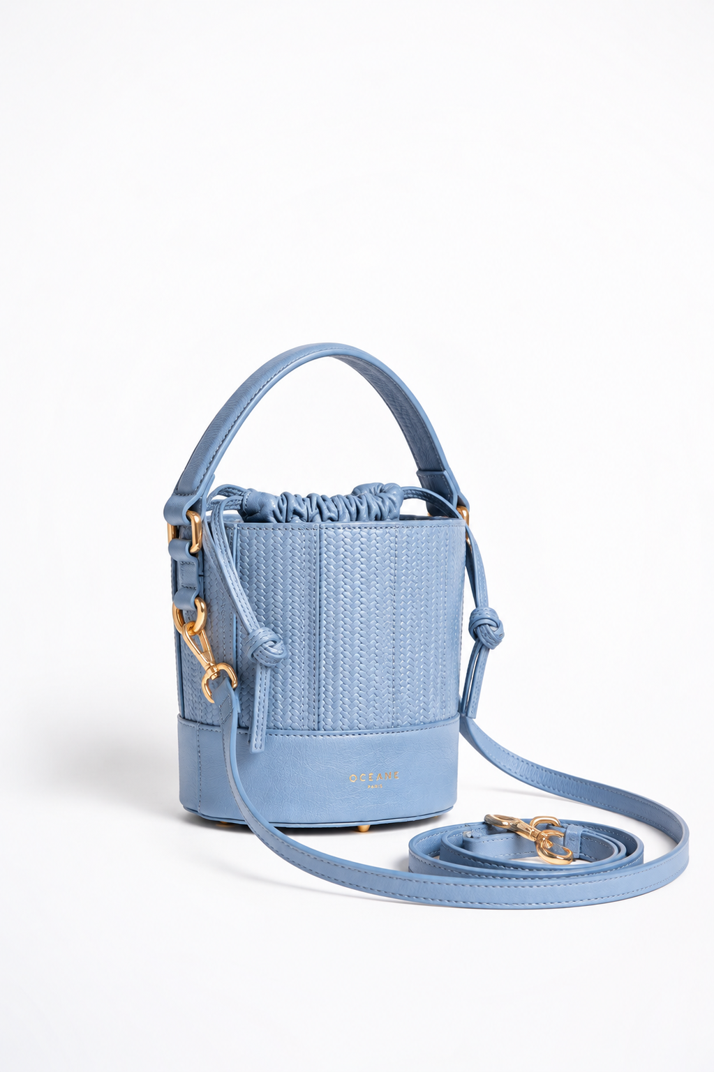 Grace Bucket azzurra di Oceane Paris, vista di tre quarti con manico in pelle e tracolla appoggiata accanto alla borsa.